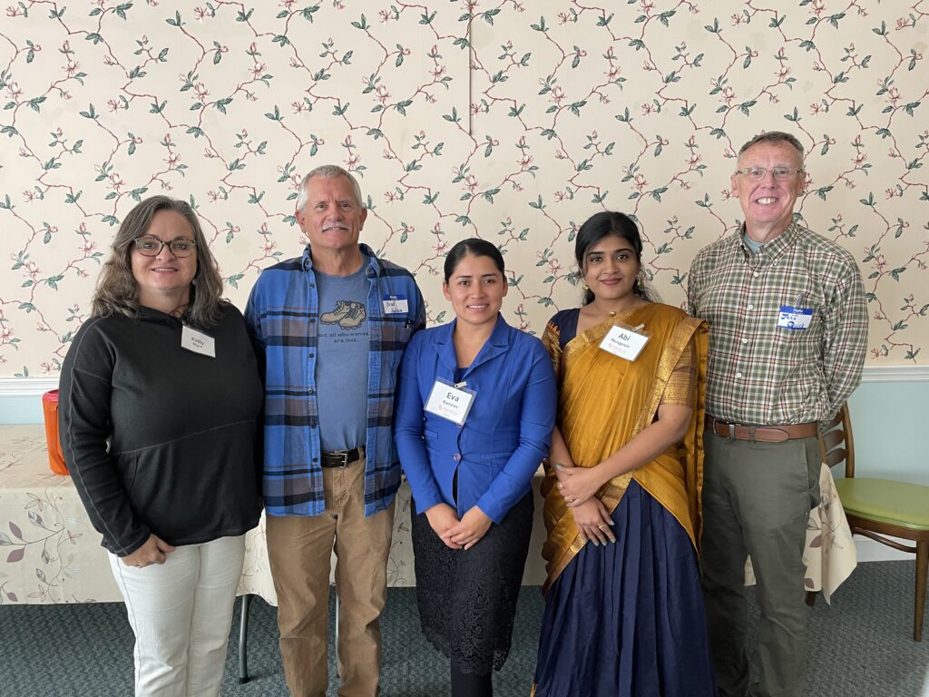 Five people stand in a row in front of a wall. 