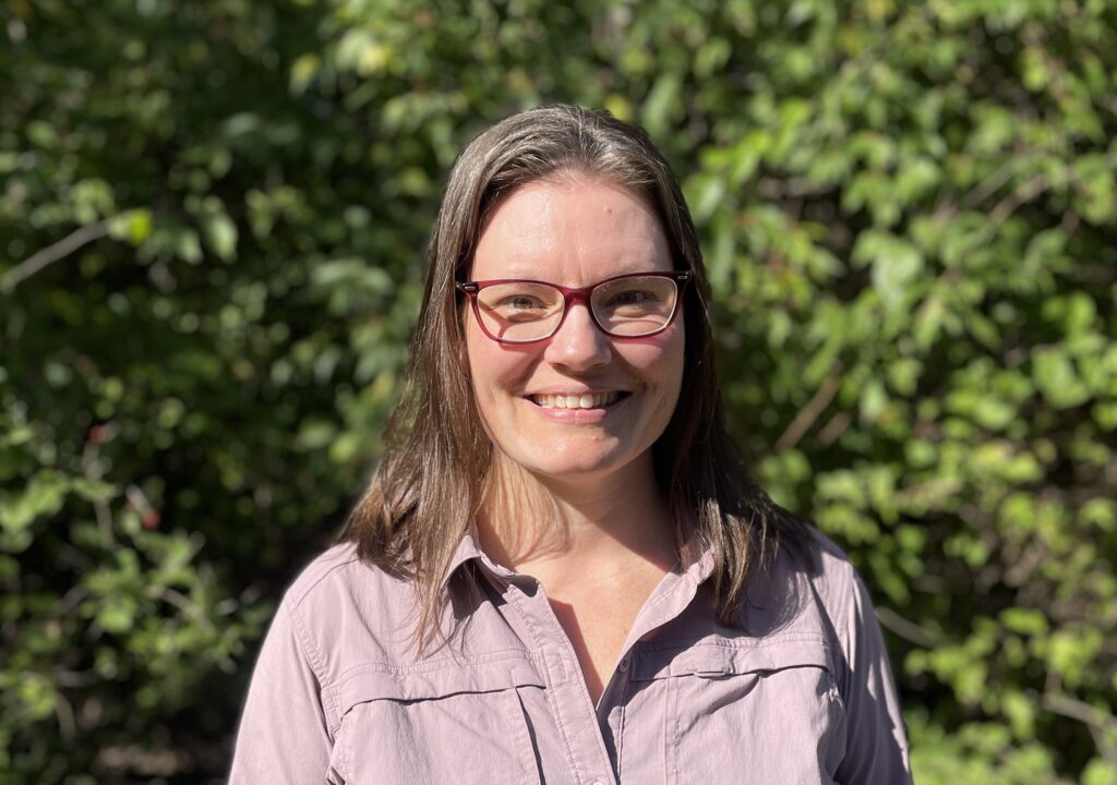 Sarah stands in front of greenery 