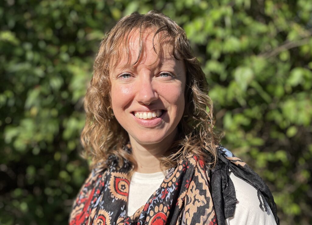 Emily stands in front of greenery 