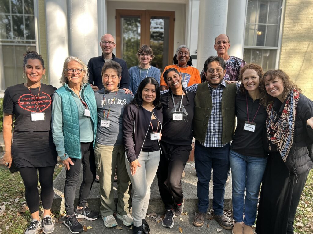 A group of fourteen people stand in rows in front of a yellow building.