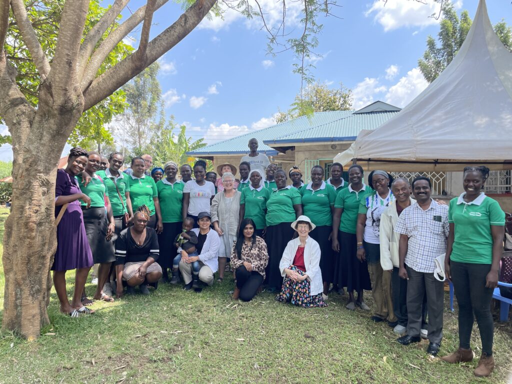 A large group of people stand together in front of a home. Many in the group where matching green polo shirts. 