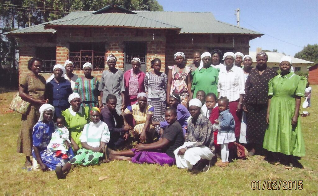 A large group of women and some children stand in front of a home