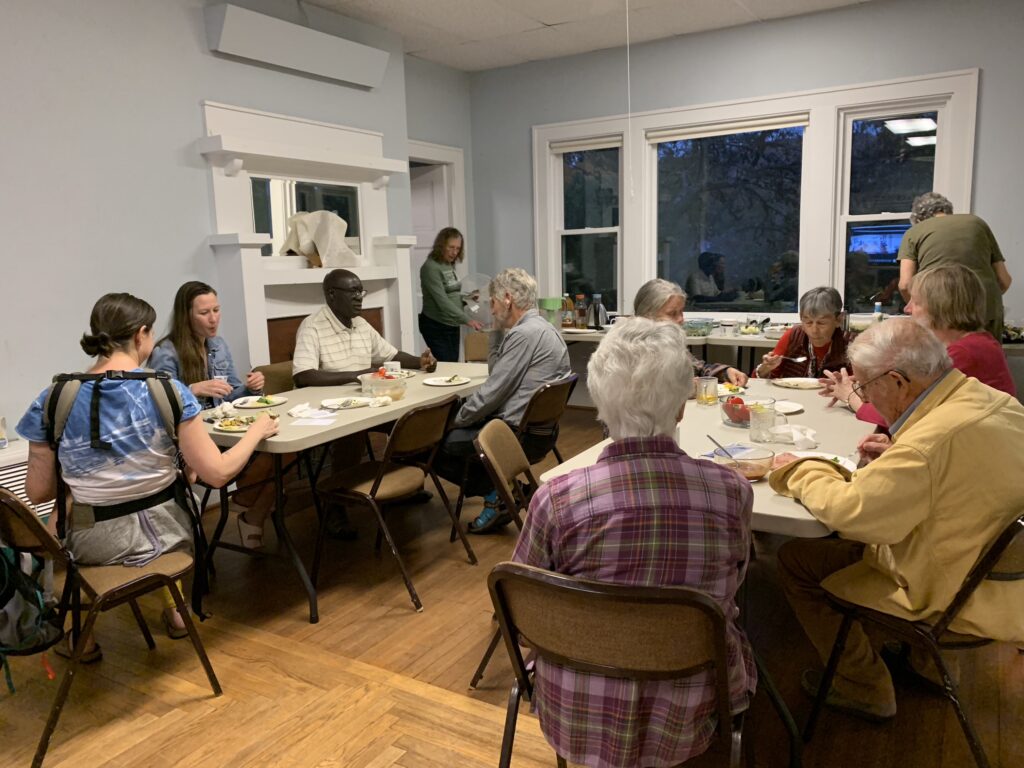 A group of people sit around two tables while they eat. 