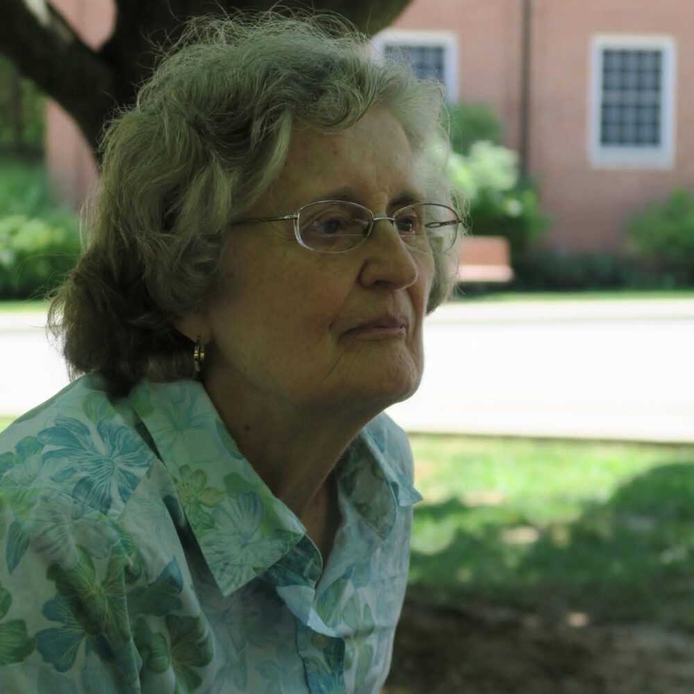 A woman sits on a chair on a grassy lawn