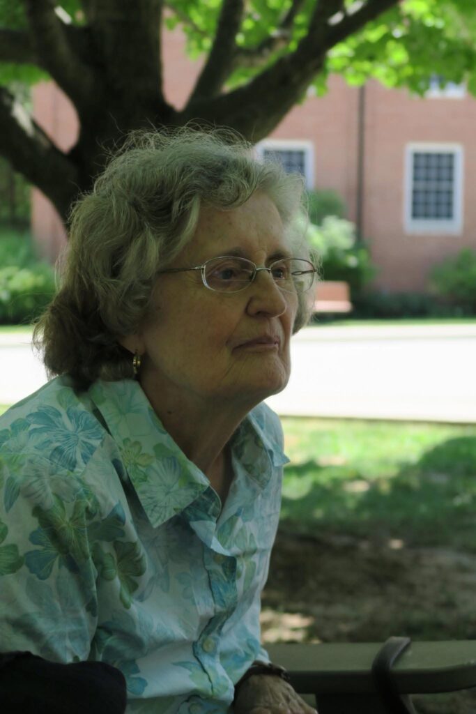 A woman sits in the shade on a grassy lawn