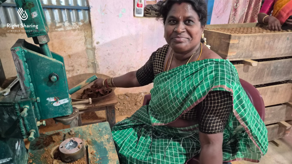 A woman wearing a green sari sits in front of a clay press 
