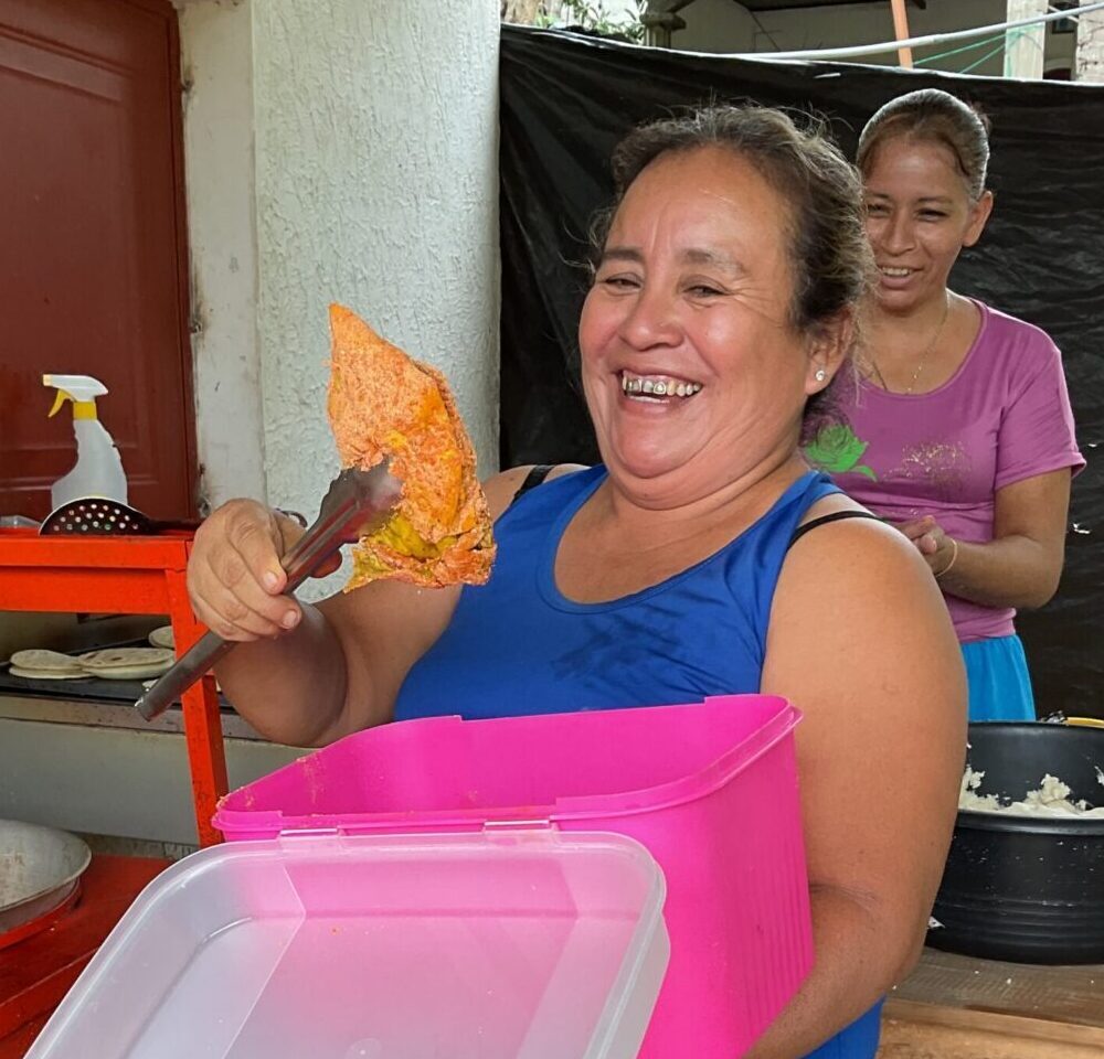 A woman holds up a piece of chicken with tongs. It appears she is about to place it in a fryer.