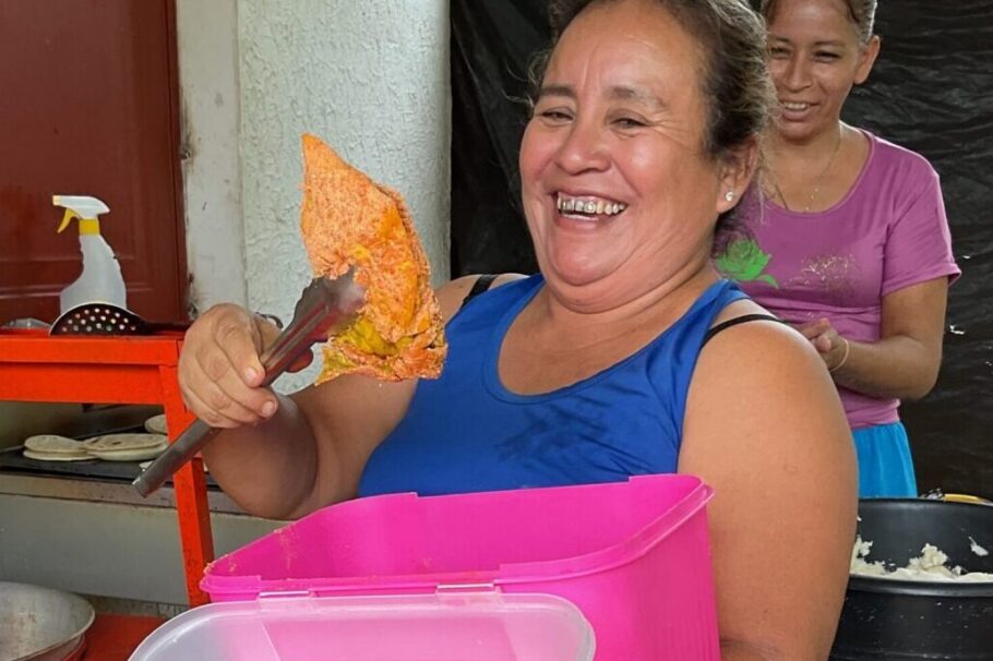 A woman holds up a piece of chicken with tongs. It appears she is about to place it in a fryer.