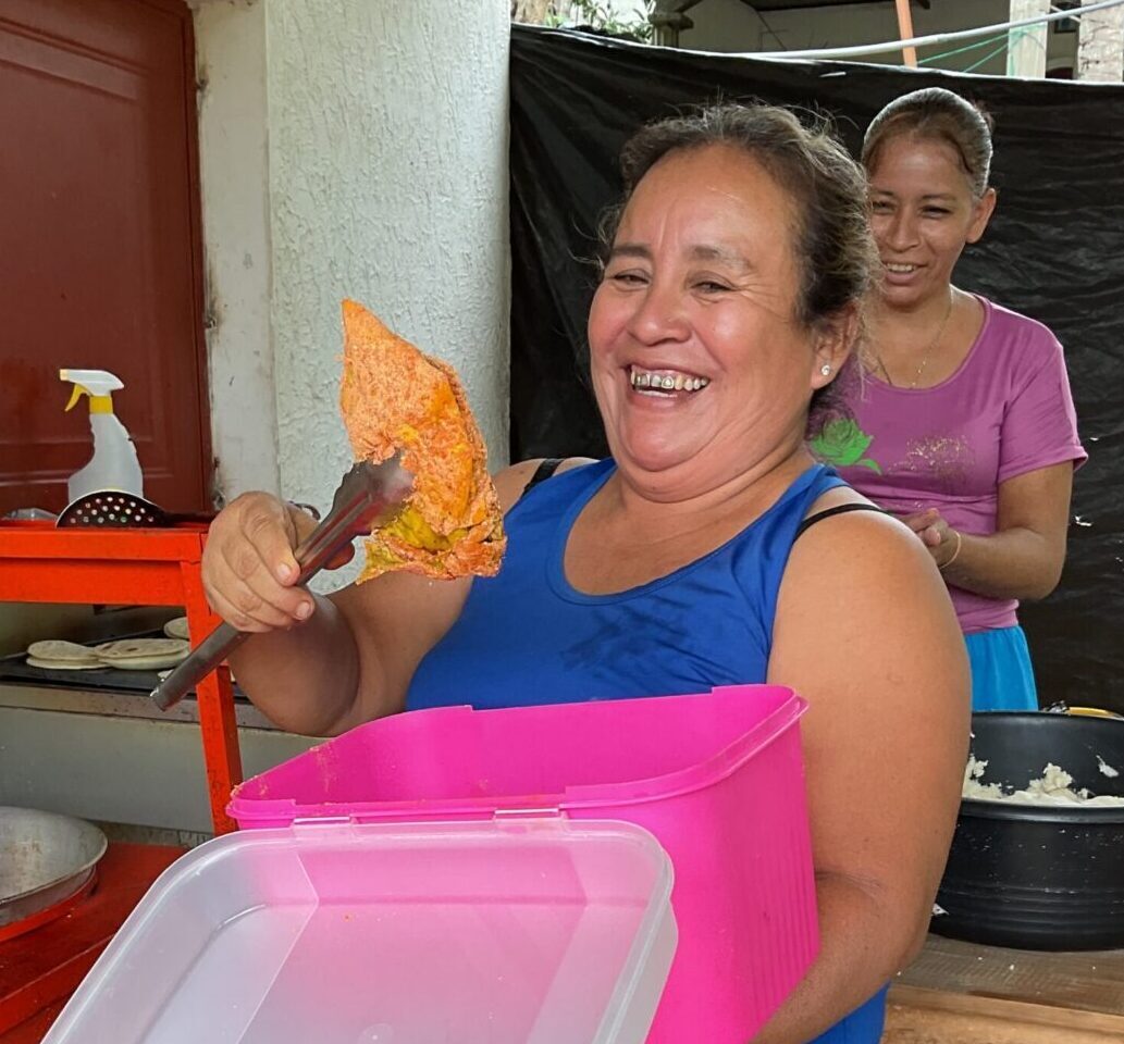 A woman holds up a piece of chicken with tongs. It appears she is about to place it in a fryer.