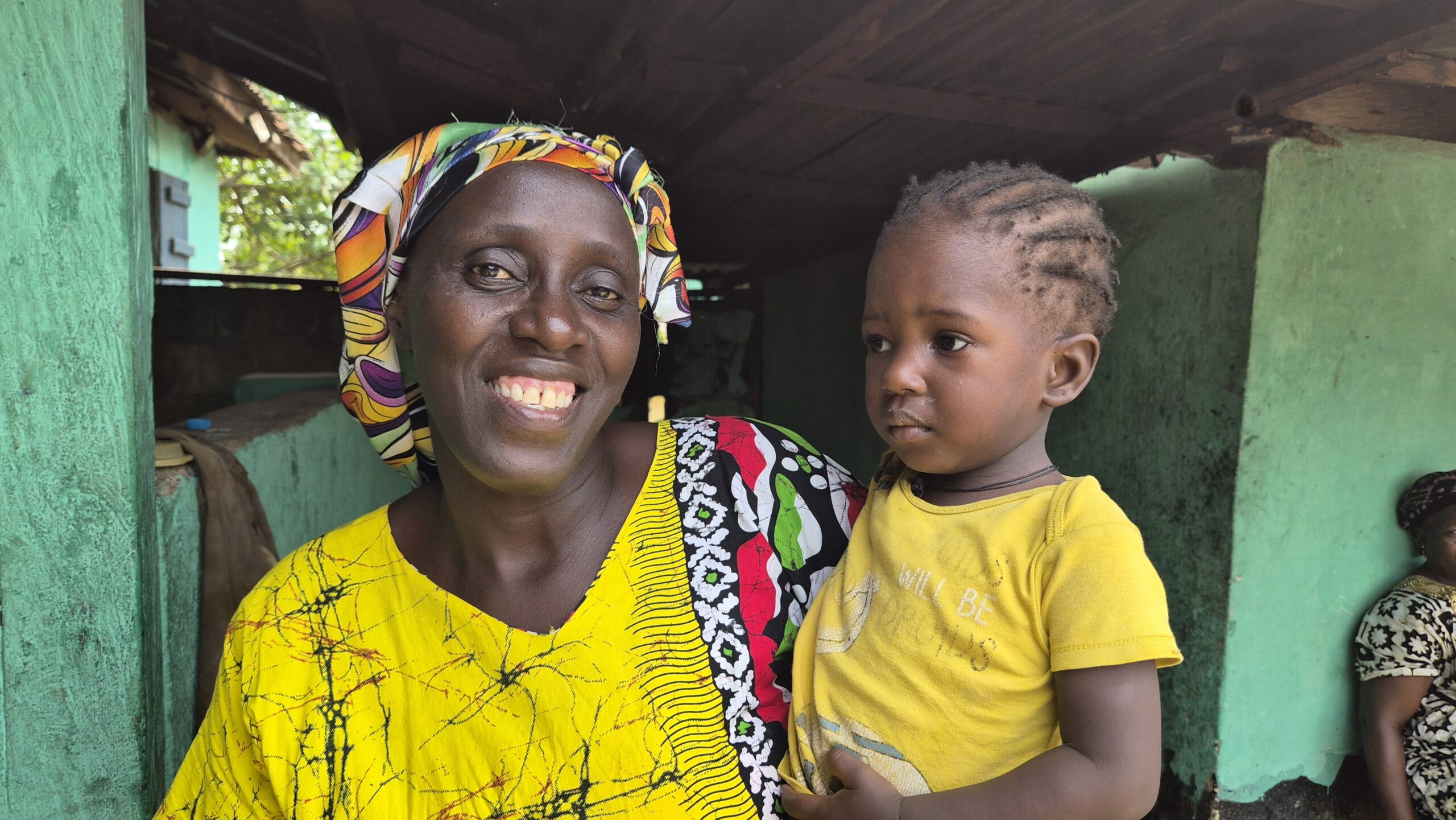 A woman wears a yellow dress while holding her child.