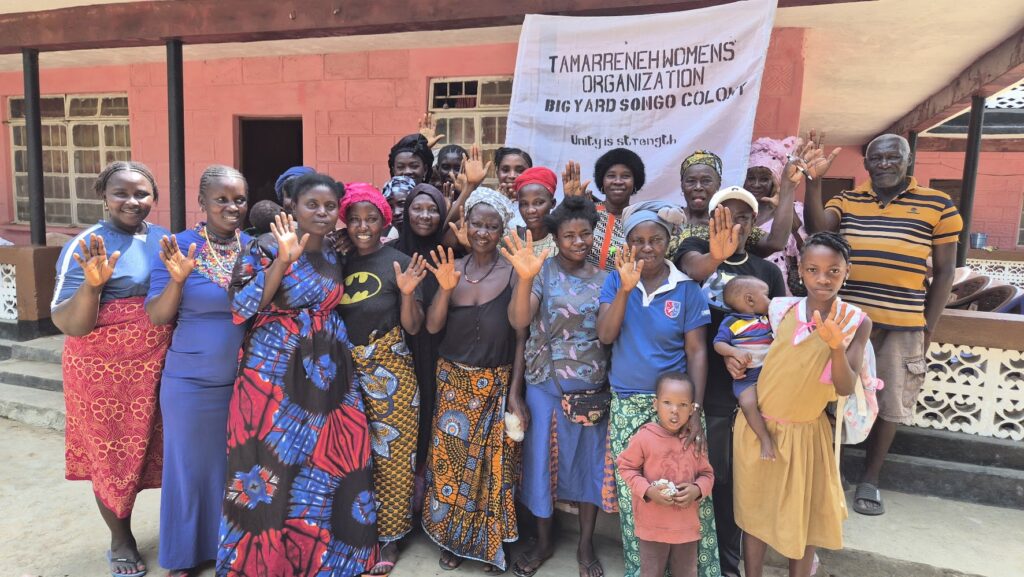 A large group of women stand in front of a building with a sign behind them that reads Tamarreneh Women's Organization.