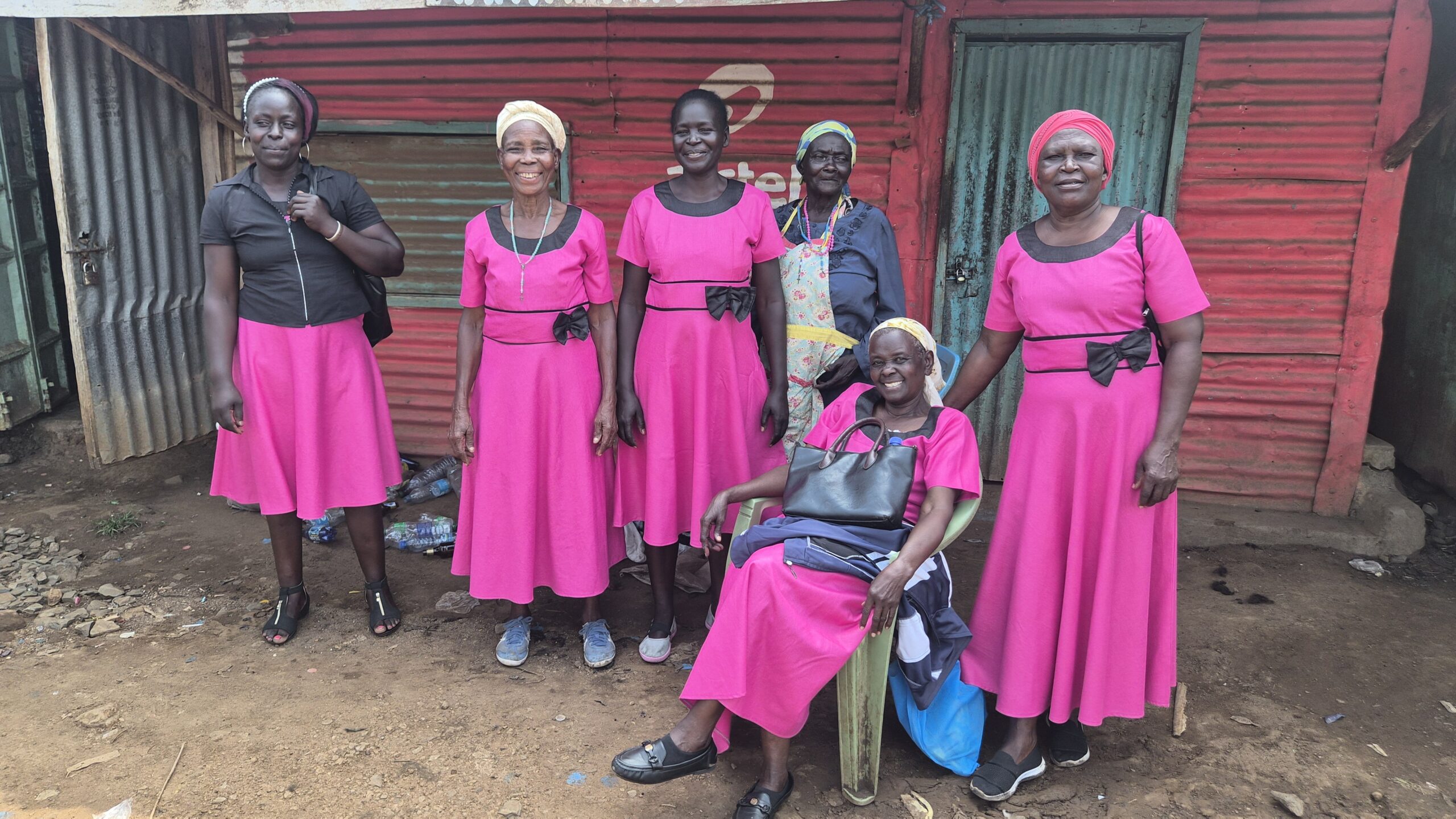 A group of women wearing bright pink dresses stand together,